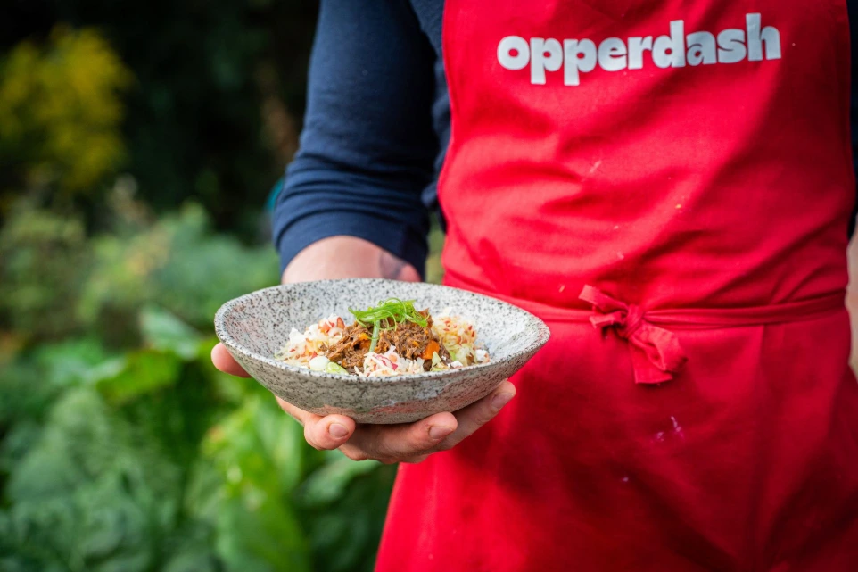Elias Nys en tablier Opperdash tenant une assiette du service traiteur